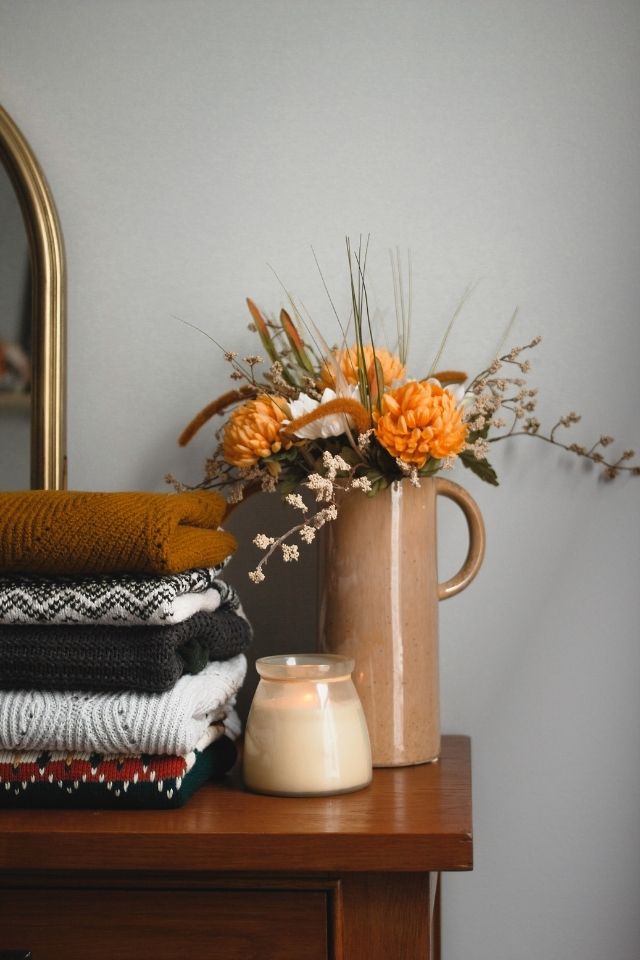 Thanksgiving decor flower arrangement on top of dresser with candles and orange flowers 